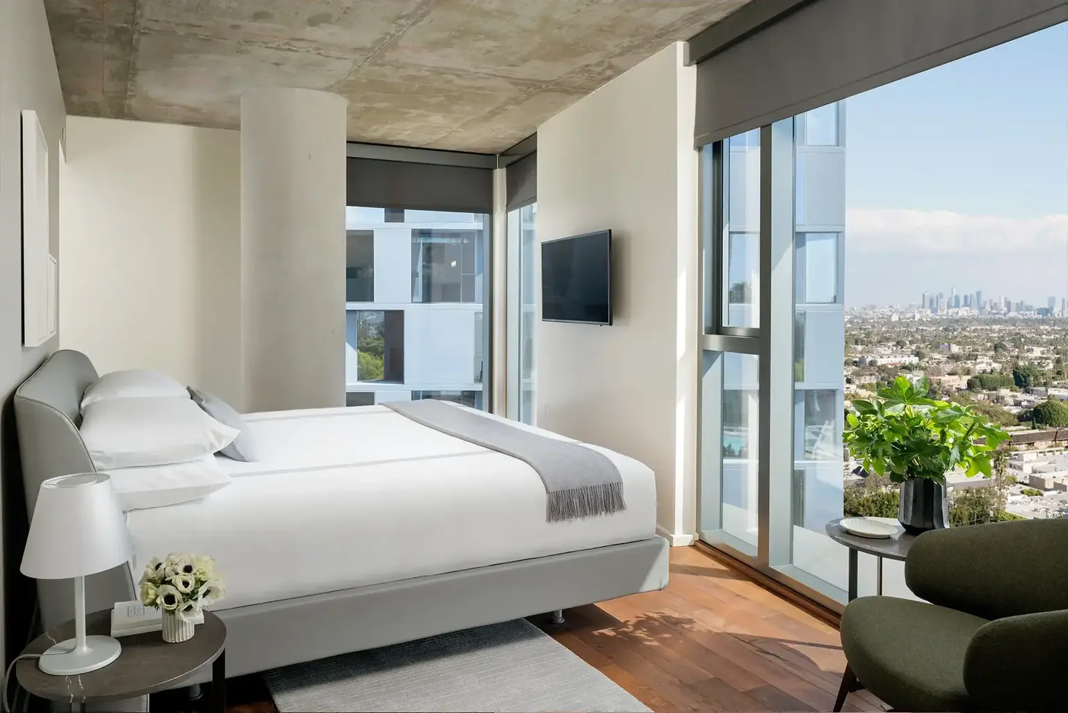 AKA West Hollywood apartment bedroom with concrete ceiling and king bed with large window view of city  