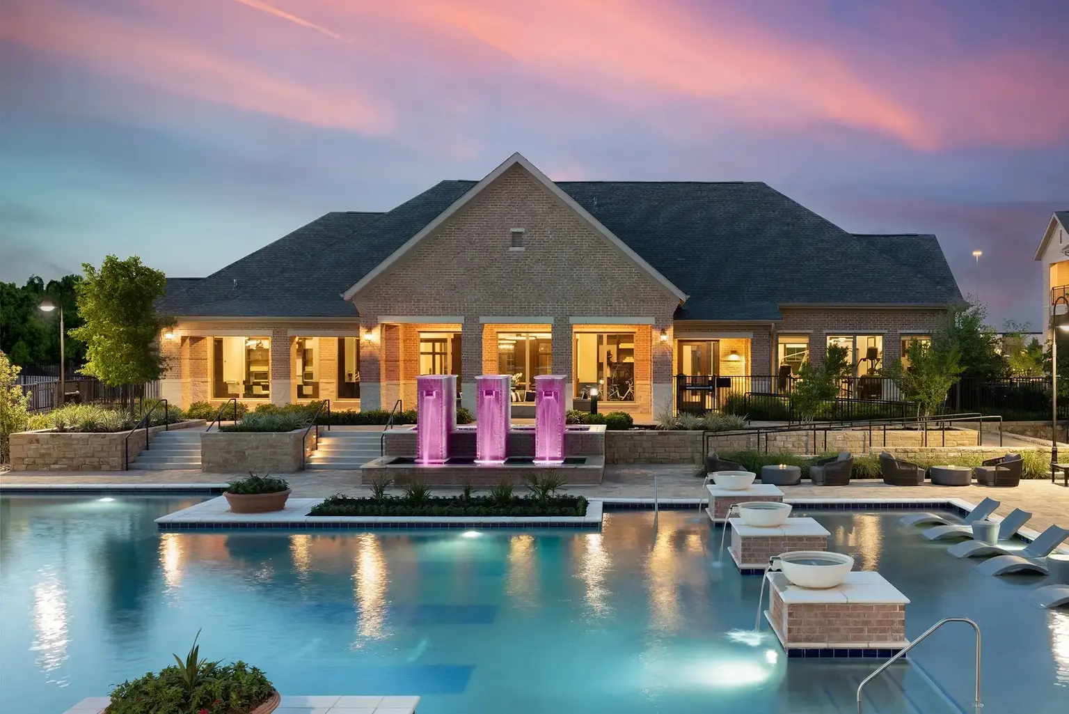 AVE Las Colinas Pool at dusk with illuminated waterfalls and comfortable lounge chairs