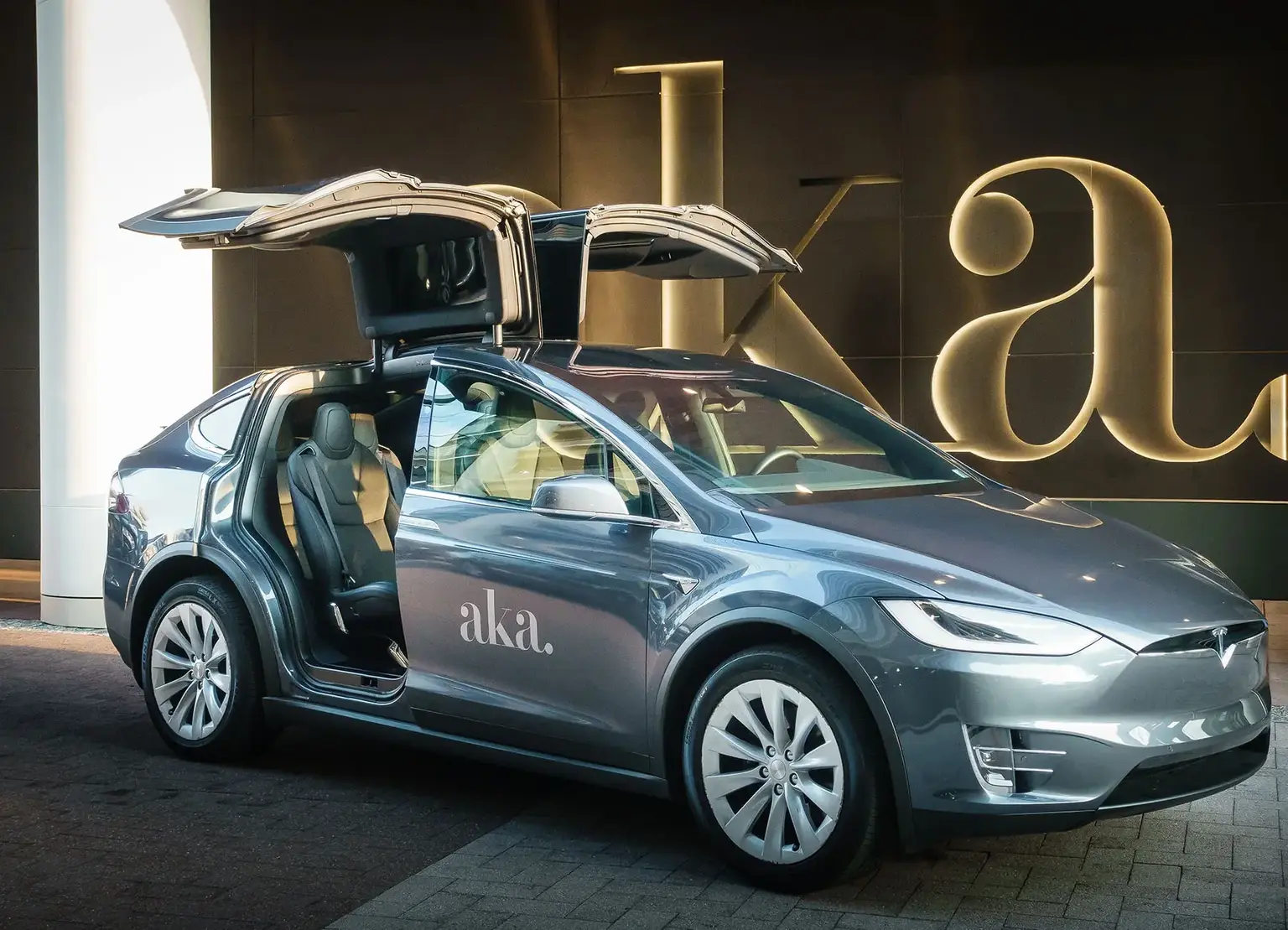 AKA branded Tesla in front of exterior entrance with AKA sign outside AKA University City